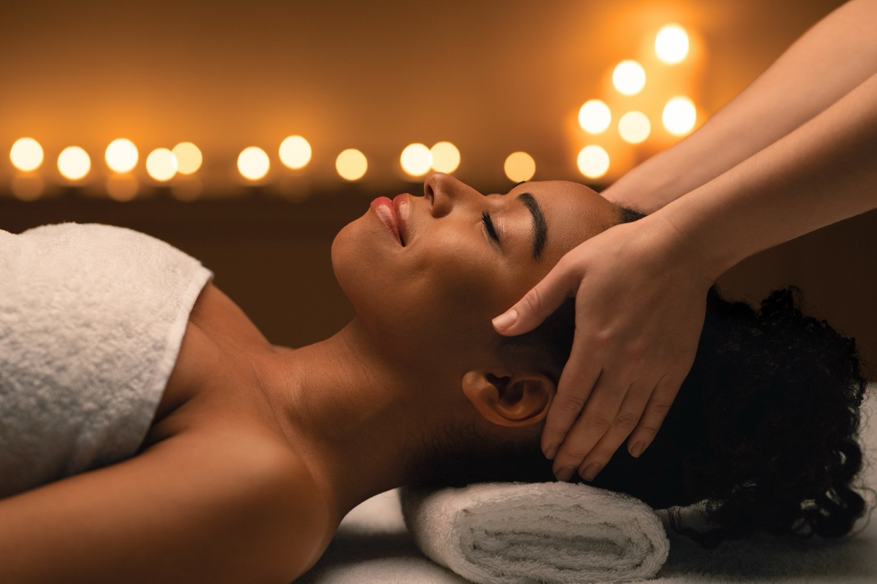 Young african lady enjoying head massage at spa decorated with candles, closeup